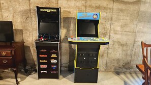 Två arkadspel, ett för Legends Ultimate Mini och ett annat för The Simpsons, placerade framför en vägg med en tydlig struktur.