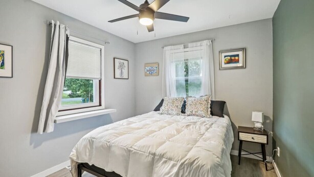 A bedroom with a bed, a ceiling fan, a nightstand, and a window with curtains.