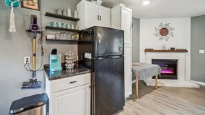 A kitchen with a black refrigerator, white cabinets, a coffee machine, and a fireplace.