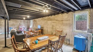 A basement with a wooden dining table, chairs, a sofa, and a window.