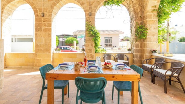 A dining area with a wooden table and chairs, surrounded by stone arches and greenery. - 4005 Villetta Stella by Barbarhouse (Manduria)