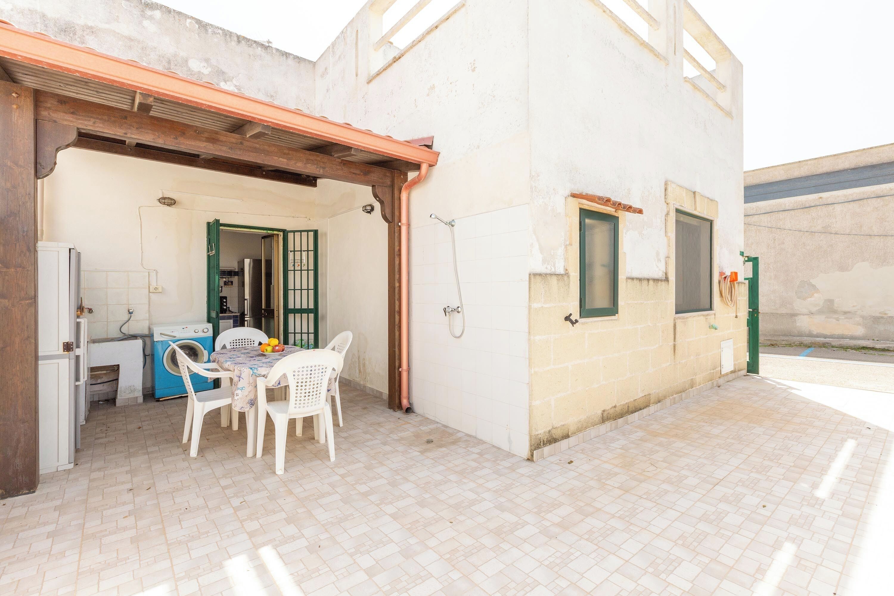 Un petit bâtiment d’un seul étage, doté d’une terrasse carrelée, d’un lave-linge et d’une table avec des chaises.