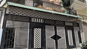 A building with a black and white facade, decorative metal railings, and a green awning. - OYO 1248 Quyen House (Cam Ly - Da Lat)