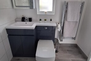 Une salle de bain moderne avec un lavabo blanc, des meubles sombres, des toilettes et un porte-serviettes.