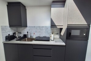 Una cocina compacta con armarios oscuros, un lavamanos de acero inoxidable, una cafetera, un microondas y un tostador.