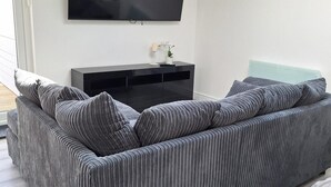A modern living room with a grey sofa, a black entertainment unit, and a light blue accent wall. - Lodge - Sleeps 2 - Pet Friendly - Parking - Patio (Sidcup)