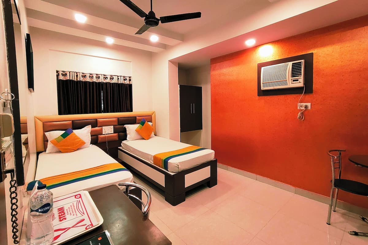 Une chambre d’hôtel avec deux lits, un ventilateur de plafond, un appareil de climatisation et une petite table sur laquelle se trouvent une bouteille d’eau et un menu.