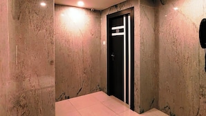 A modern elevator with a black door and white stripes, surrounded by marble walls and a shiny tiled floor. - HOTEL STEAM (Kolkata)