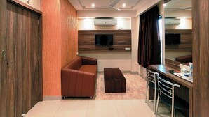 A modern living room with a sofa, a coffee table, a TV mounted on the wall, and a ceiling fan. - HOTEL STEAM (Kolkata)
