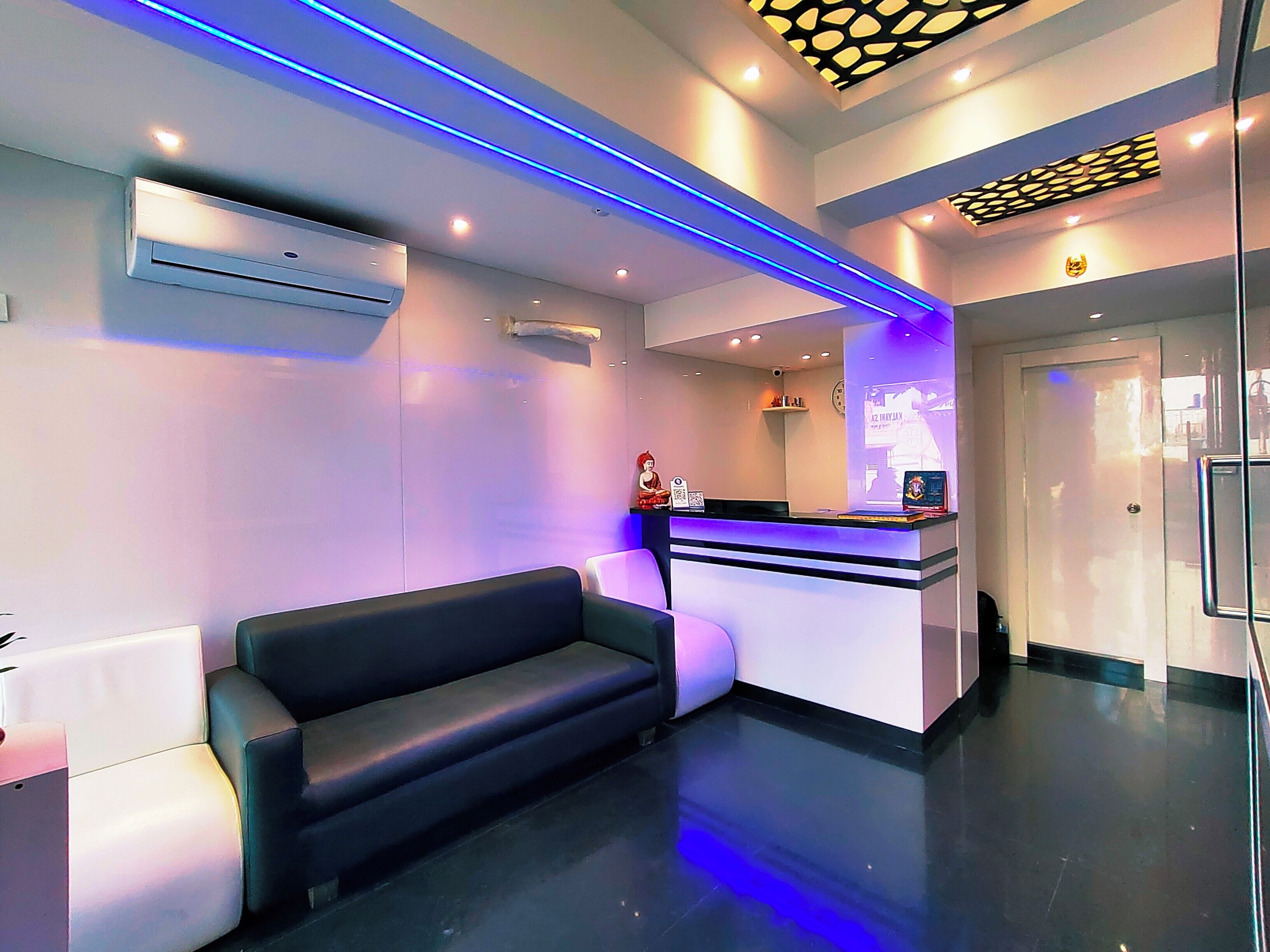 A modern reception area with a black leather sofa, a reception desk, and a digital screen displaying information.