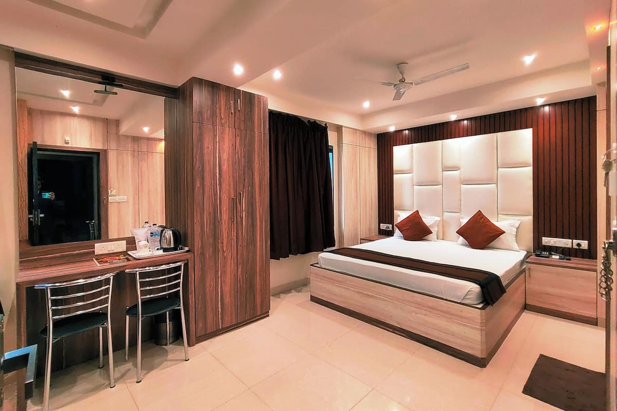 Une chambre d’hôtel moderne avec un grand lit, un bureau avec des chaises, un miroir et un ventilateur de plafond.