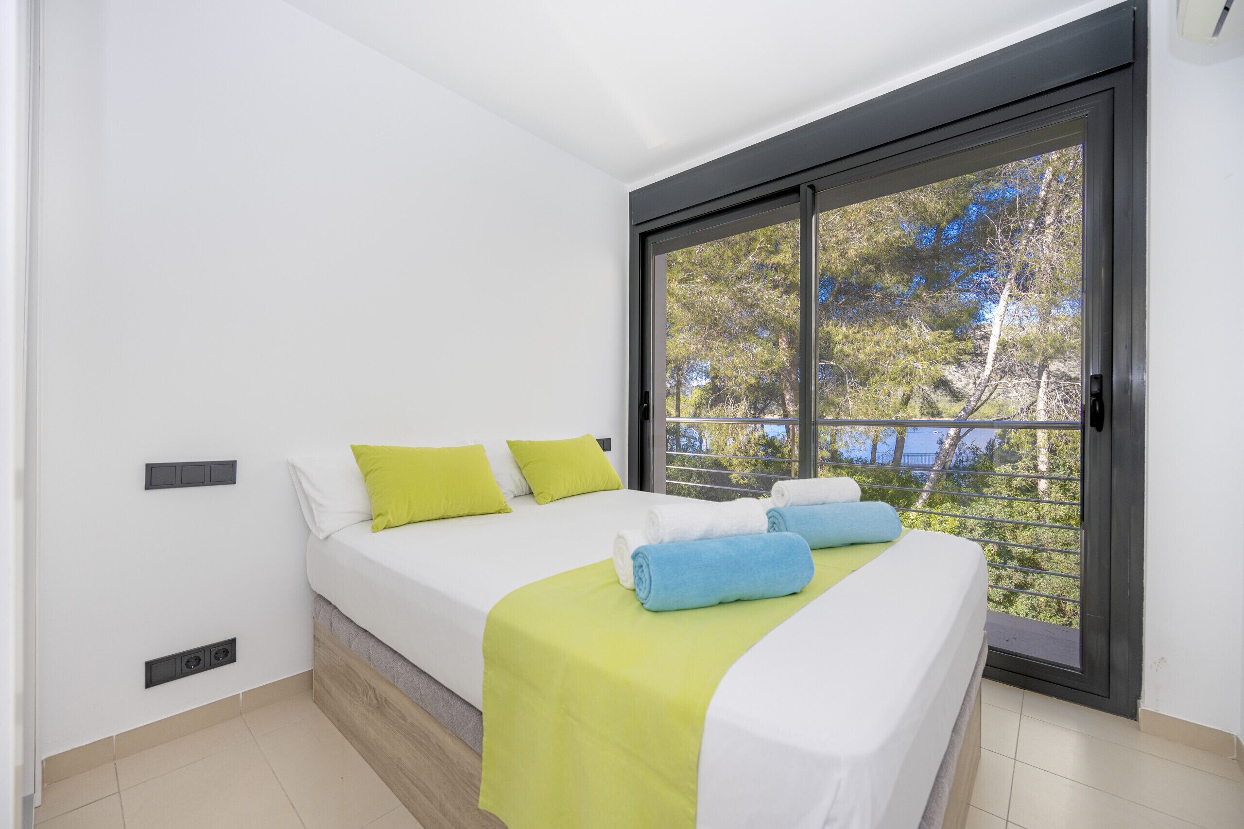 Ein Schlafzimmer mit zwei Betten, einem großen Fenster mit Blick auf Bäume und einer Schiebetür.