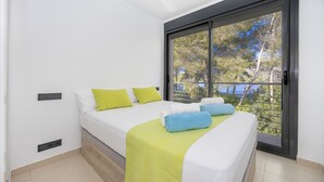 Un dormitorio con dos camas, un ventanal con vistas a árboles y una puerta corredera.