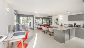 Una cocina moderna con una isla central, un comedor con sillas rojas y un amplio ventanal con vistas al exterior.
