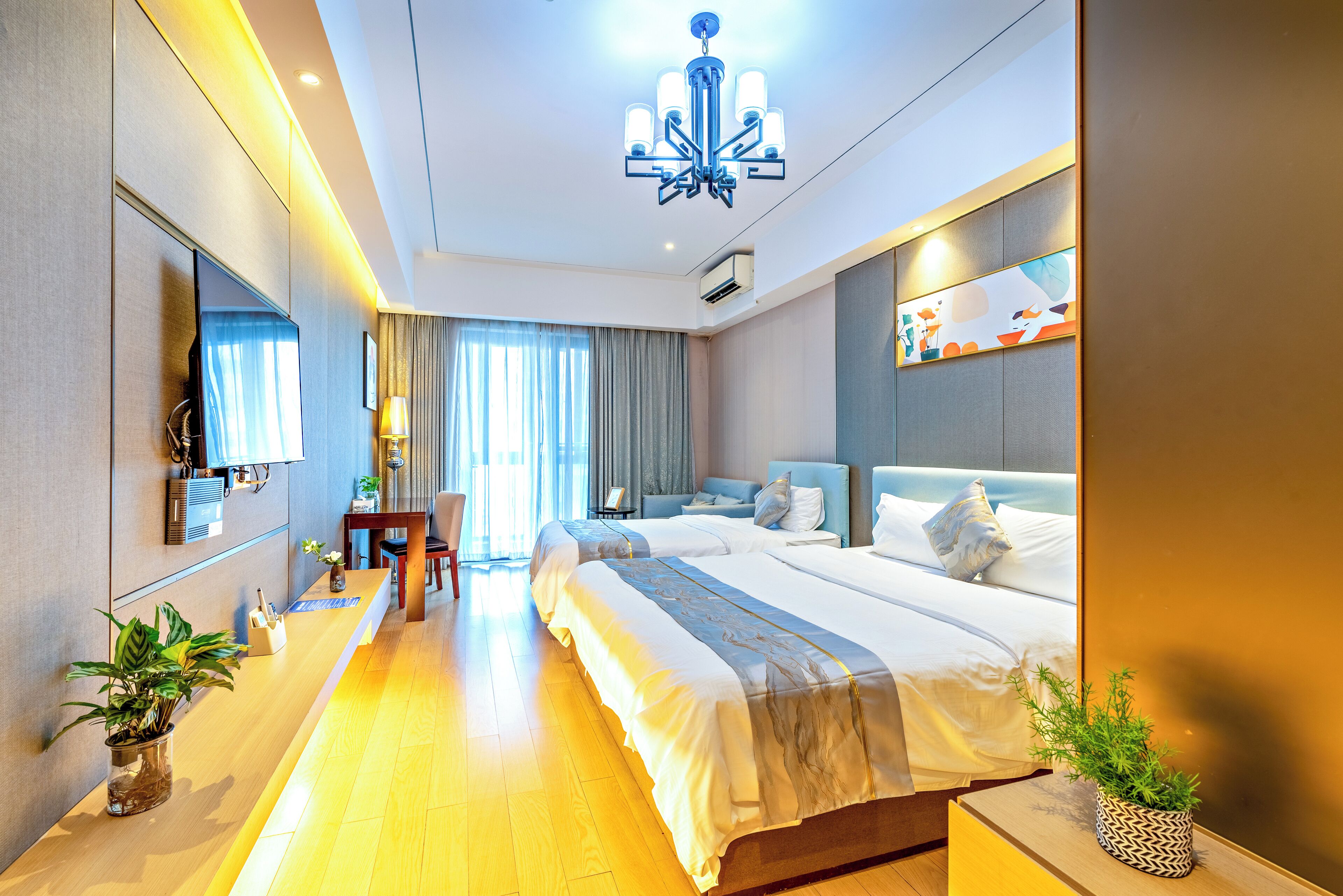 A modern hotel room with a large bed, a desk, a chair, and a potted plant.
