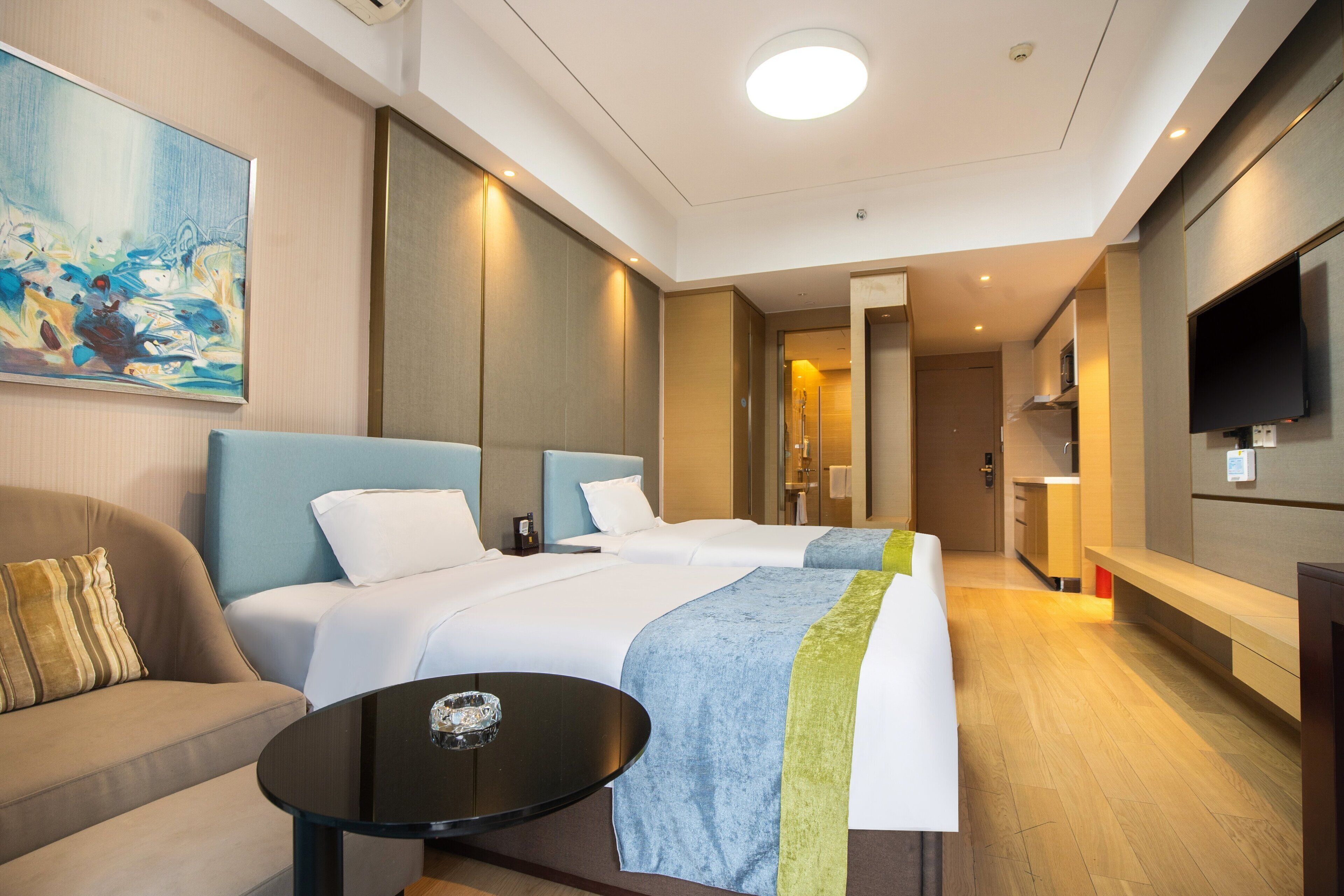 Una habitación de hotel moderna con dos camas, un sofá, un televisor y un cuadro en la pared.