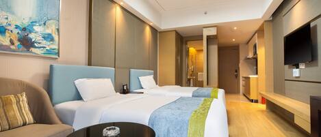 Una habitación de hotel moderna con dos camas, un sofá, un televisor y un cuadro en la pared.