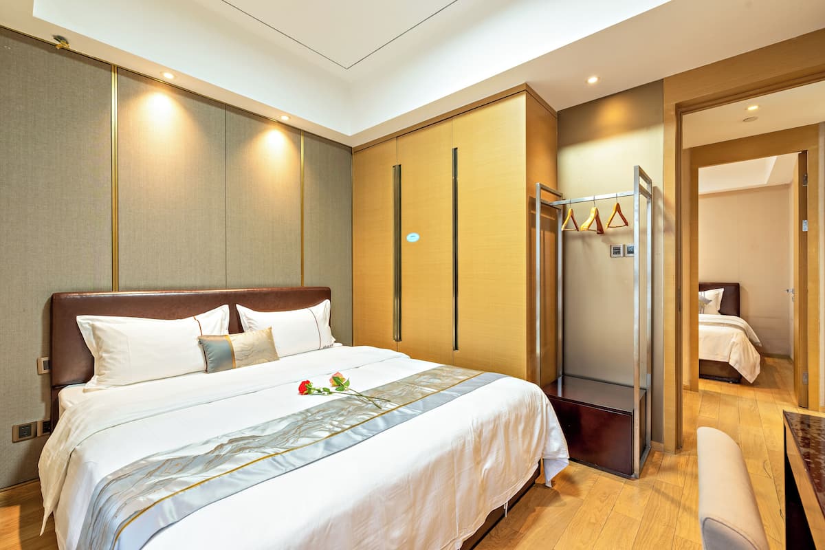A hotel room with a large bed, a wooden headboard, a wardrobe, a bench, and a clothing rack.