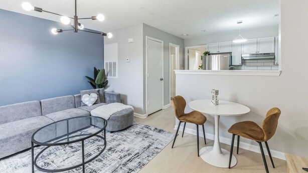 Ein modernes Wohnzimmer mit einem grauen Ecksofa, einem Glastisch und einem runden Esstisch mit zwei Stühlen.