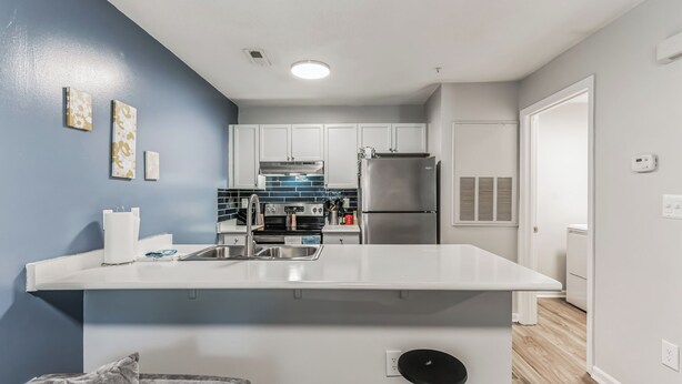 Una cucina moderna con mobili bianchi, un frigorifero in acciaio inossidabile e uno schienale blu.
