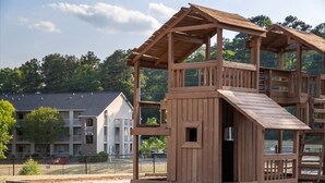 Una baita di legno con una rampa e una piccola porta, circondata da una recinzione e alberi.