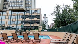 Ein Poolbereich auf dem Dach mit Liegestühlen, einem Pool und Blick auf ein Gebäude mit einem Glockenturm.