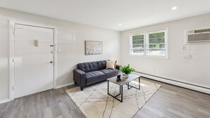 Een moderne woonkamer met een donkergrijze bank, een witte vloerkleden en een kleine tafel met een plant.