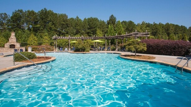 A swimming pool with clear blue water, surrounded by a wooden deck and lounge chairs.