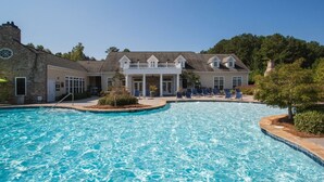 A swimming pool with lounge chairs, a stone building with a white facade, and a clear blue sky.