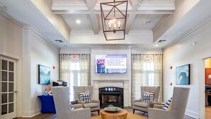 A spacious living room with a fireplace, two armchairs, a coffee table, and a television mounted on the wall.