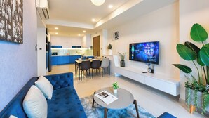 A modern living room with a blue sofa, a round coffee table, and a flat-screen TV mounted on the wall. - S Lux Apartment (Ho Chi Minh City)