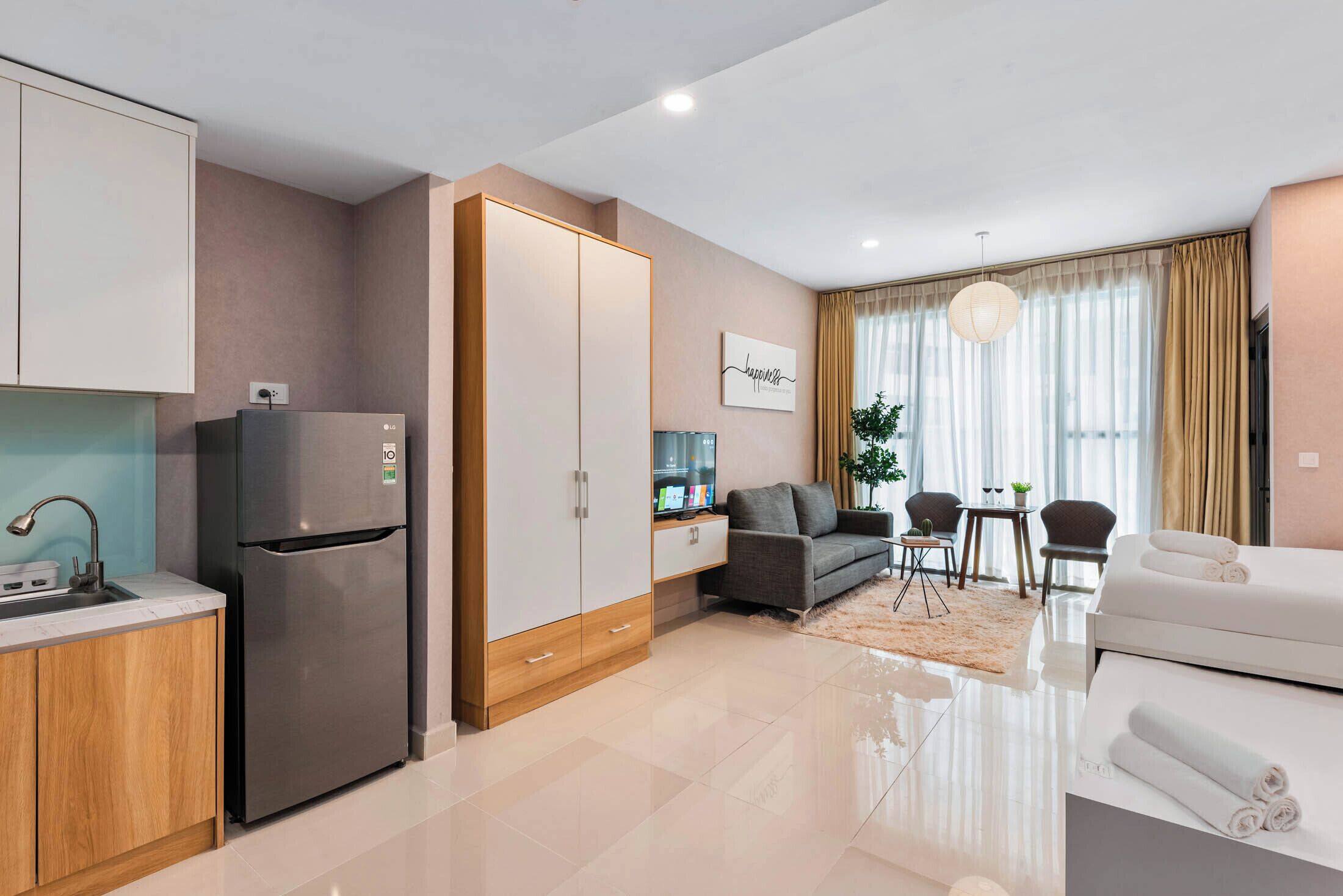 A modern hotel room with a kitchenette, a sofa, a dining area, and a large window with curtains.