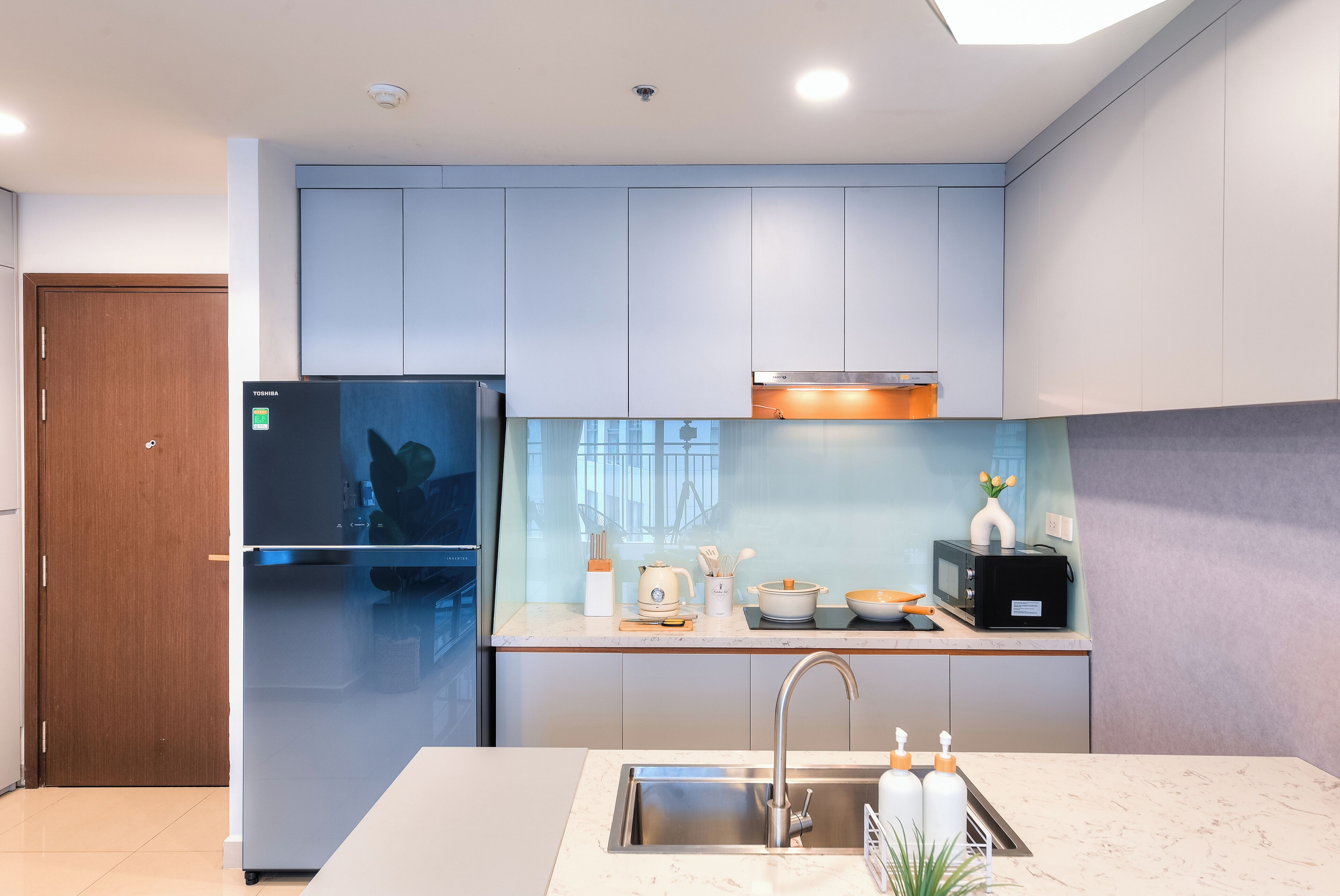 A modern kitchen with a stainless steel refrigerator, a built-in oven, a microwave, and a sink with a faucet.