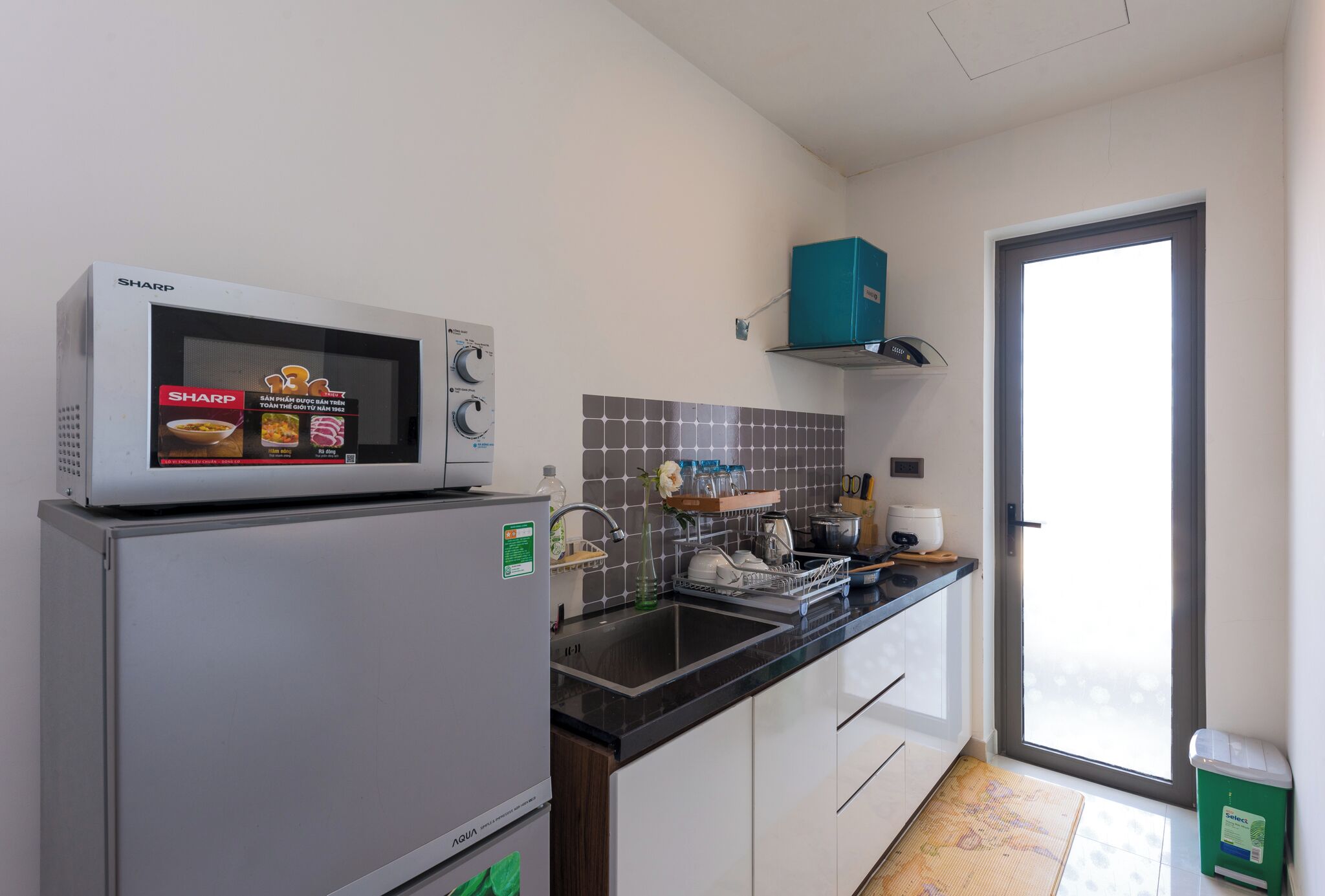 A compact kitchen with a microwave, sink, and a teal storage box.