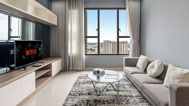 A modern living room with a large TV, a sofa, a coffee table, and a view of the city through large windows. - S Lux Apartment (Ho Chi Minh City)
