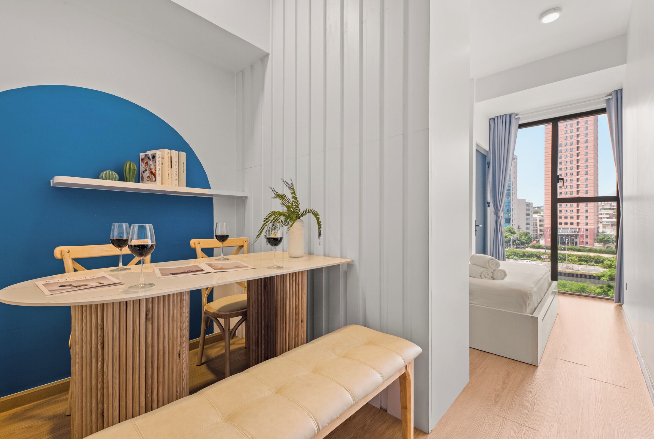 Ein modernes Zimmer mit Esstisch, Bank und Blick auf eine Stadtlandschaft durch große Fenster.