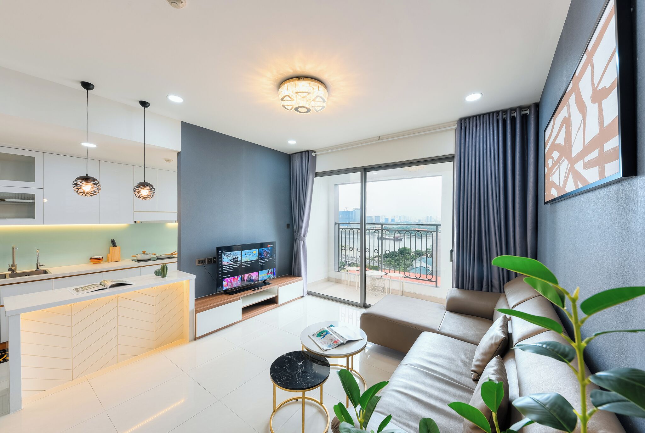 Una sala de estar moderna con un sofá, una mesa de centro y un televisor. Se observa una zona de cocina con armarios y una mesa de comedor.