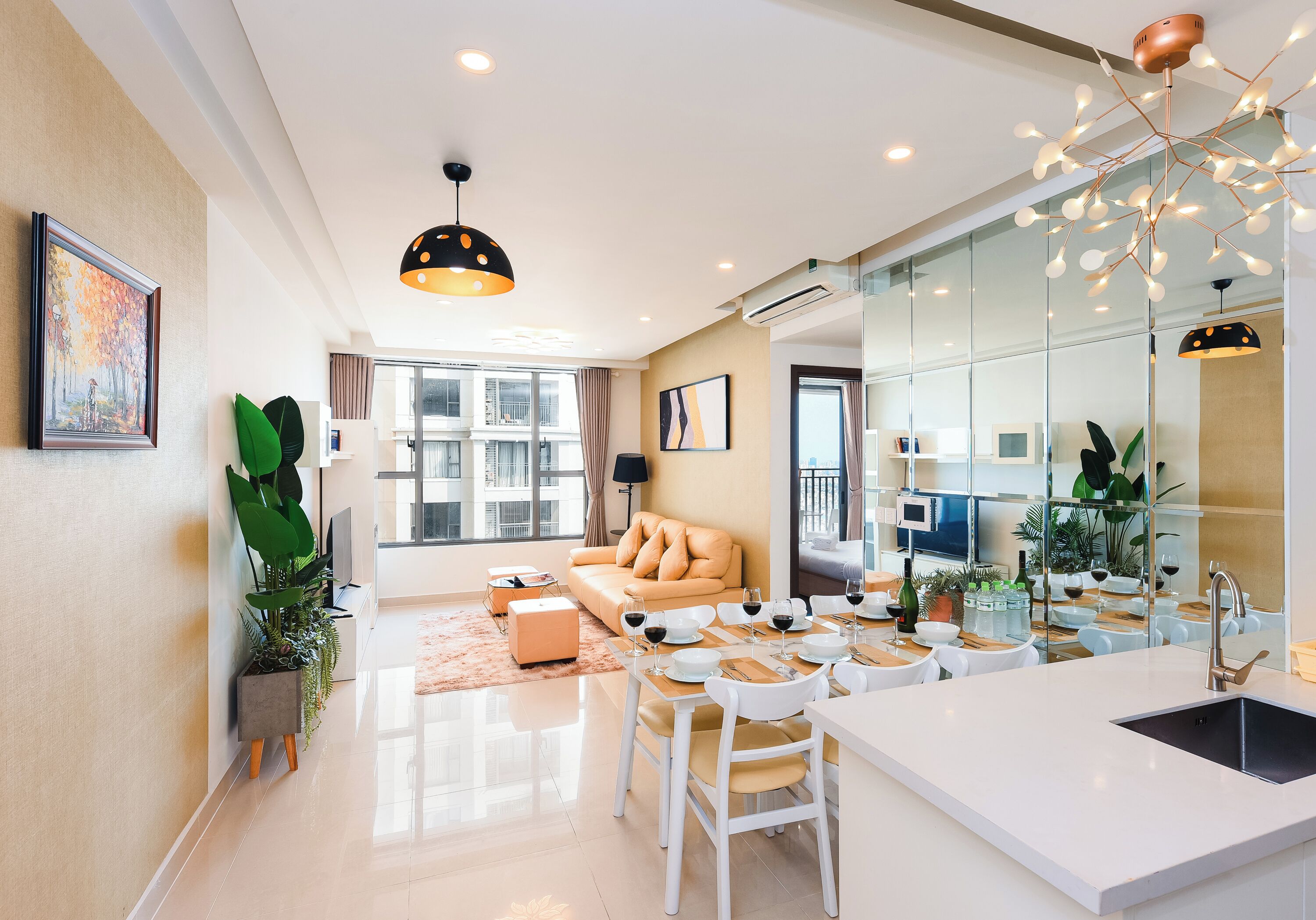 Una sala moderna con sofá, mesa de comedor y sillas, una cocina con lavaplatos y encimera, y ventanas amplias con cortinas.