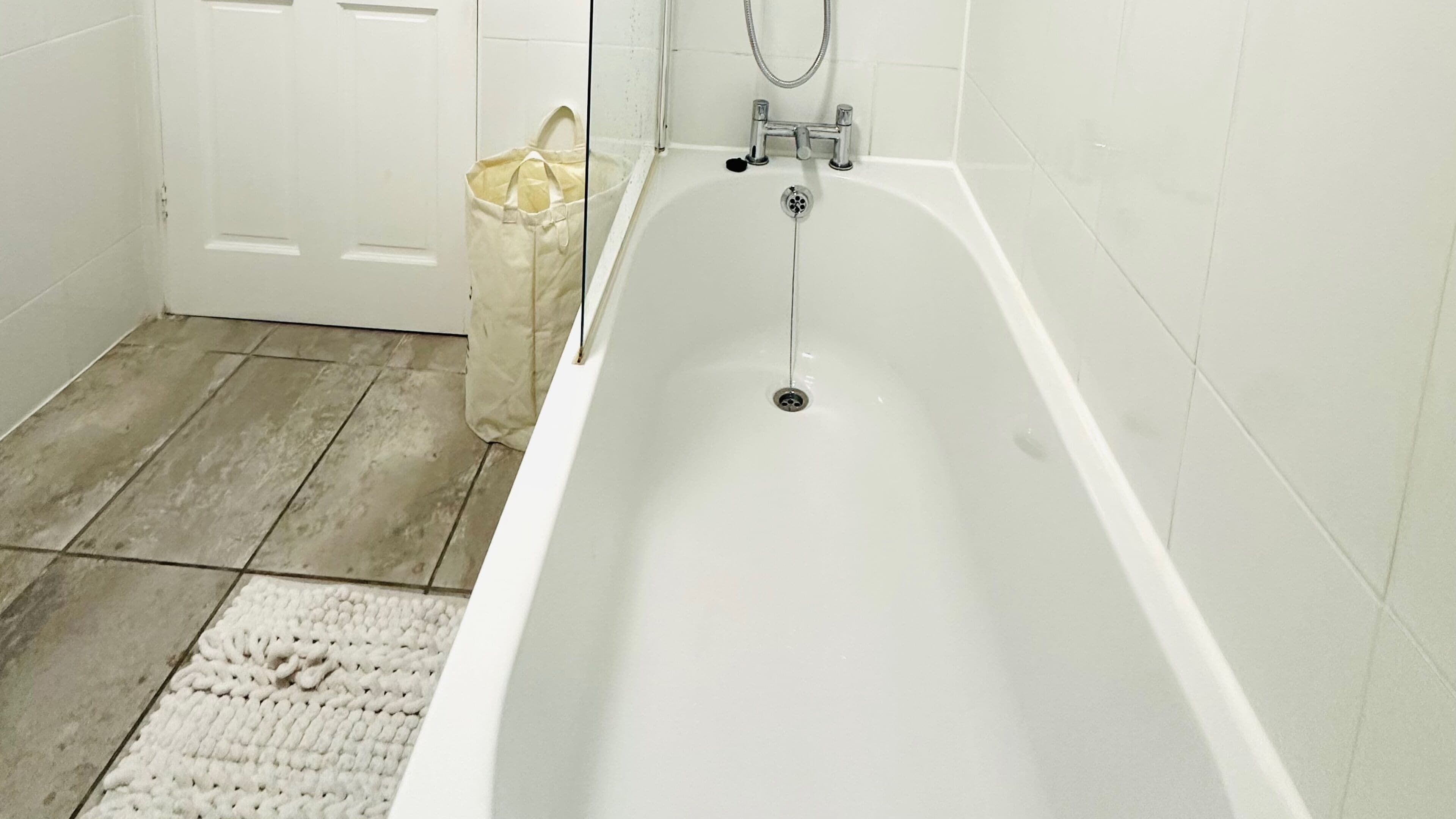 Un baño con una bañera blanca, ducha y suelo de baldosas.