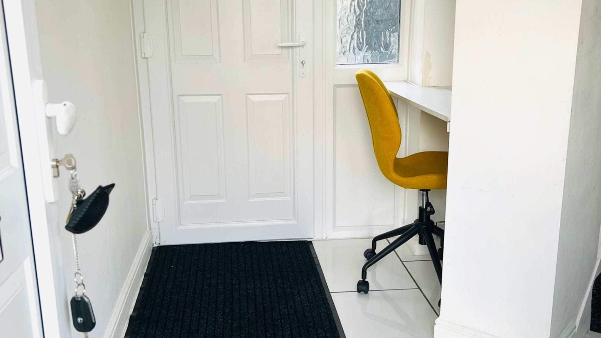 A room with a closed white door, a black doormat, a yellow office chair, and a window with a view of trees.