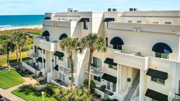 A multi-story hotel with balconies, a pool, and a view of the beach.