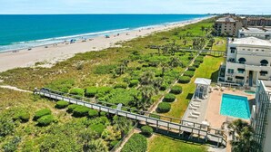 A coastal hotel with a pool, beach access, and a walking bridge over a landscaped area.