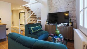 A modern living room with a sofa, a TV, and a staircase leading to an upper floor.