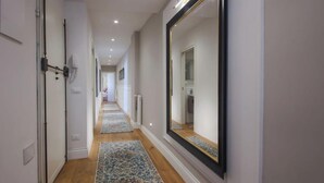 A hallway with a large mirror, a door with a handle, and a light switch on the wall.