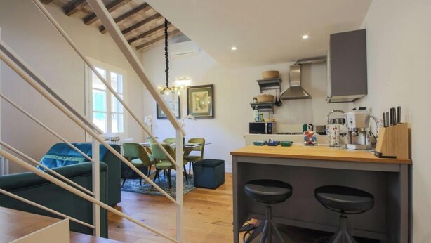 A modern kitchen with a wooden island, bar stools, and a dining area with green chairs.