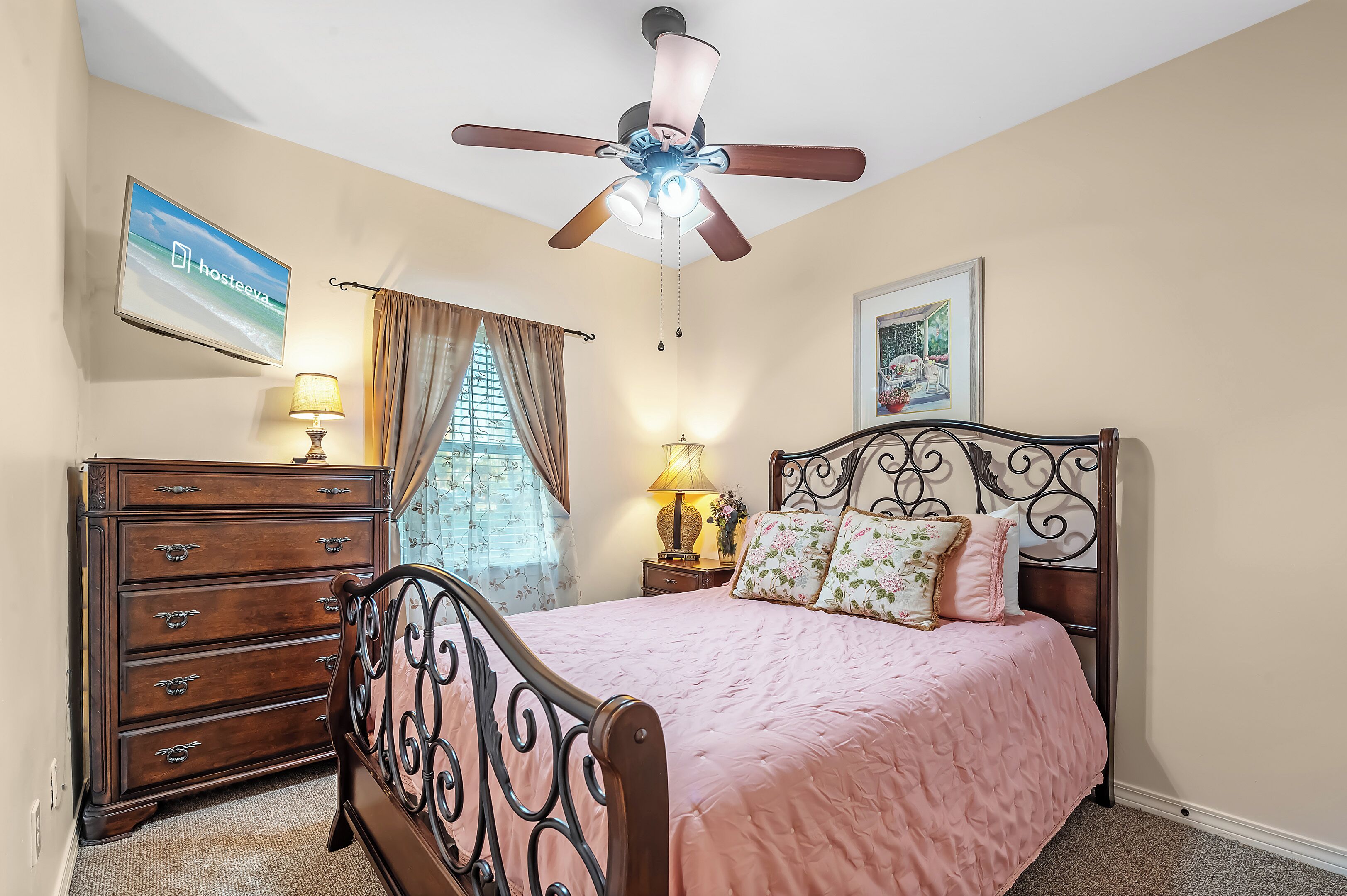 A bedroom with a bed, dresser, ceiling fan, and a TV on the wall.