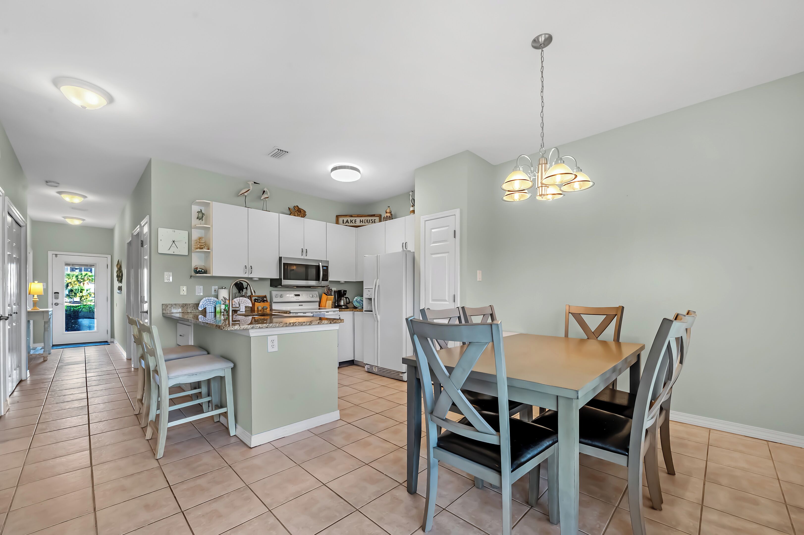 A modern kitchen with white cabinets, a central island, and a dining area with a wooden table and chairs.