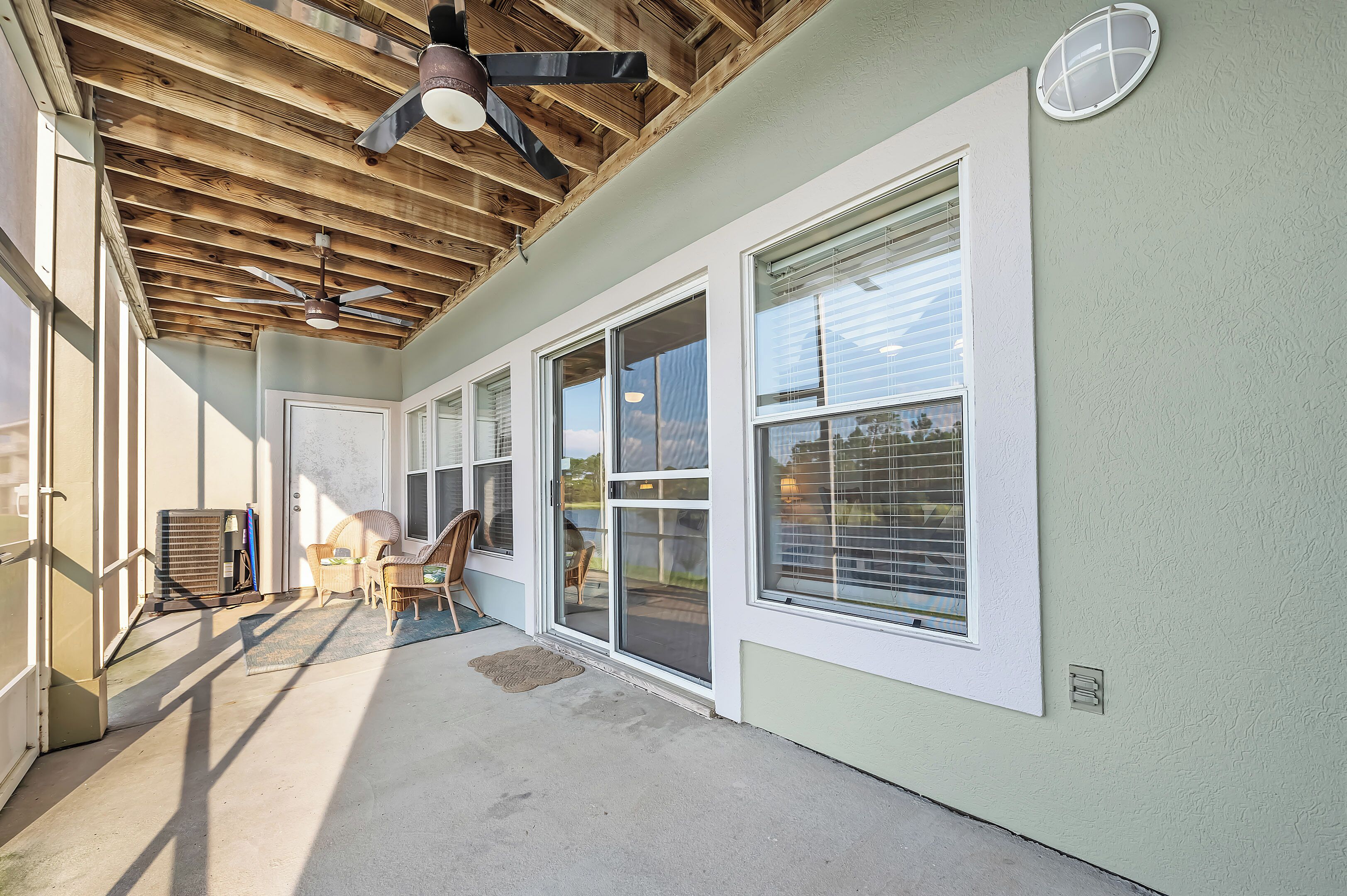 A covered patio area with a ceiling fan, large windows, and a concrete floor.