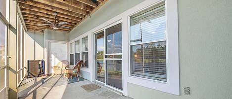 A covered patio area with a ceiling fan, large windows, and a concrete floor.