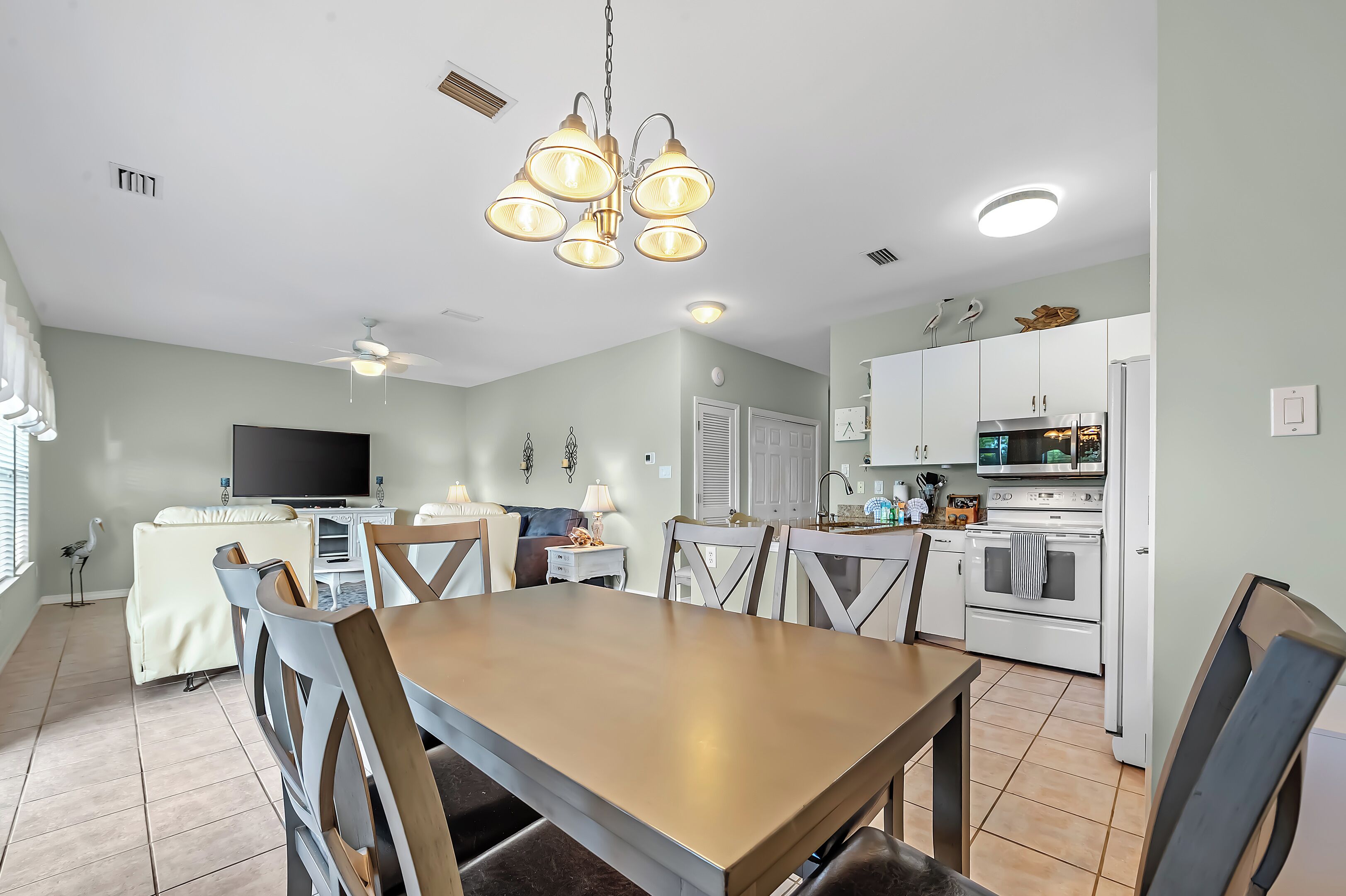 A dining area with a wooden table and chairs, a television, and a kitchen with white appliances.